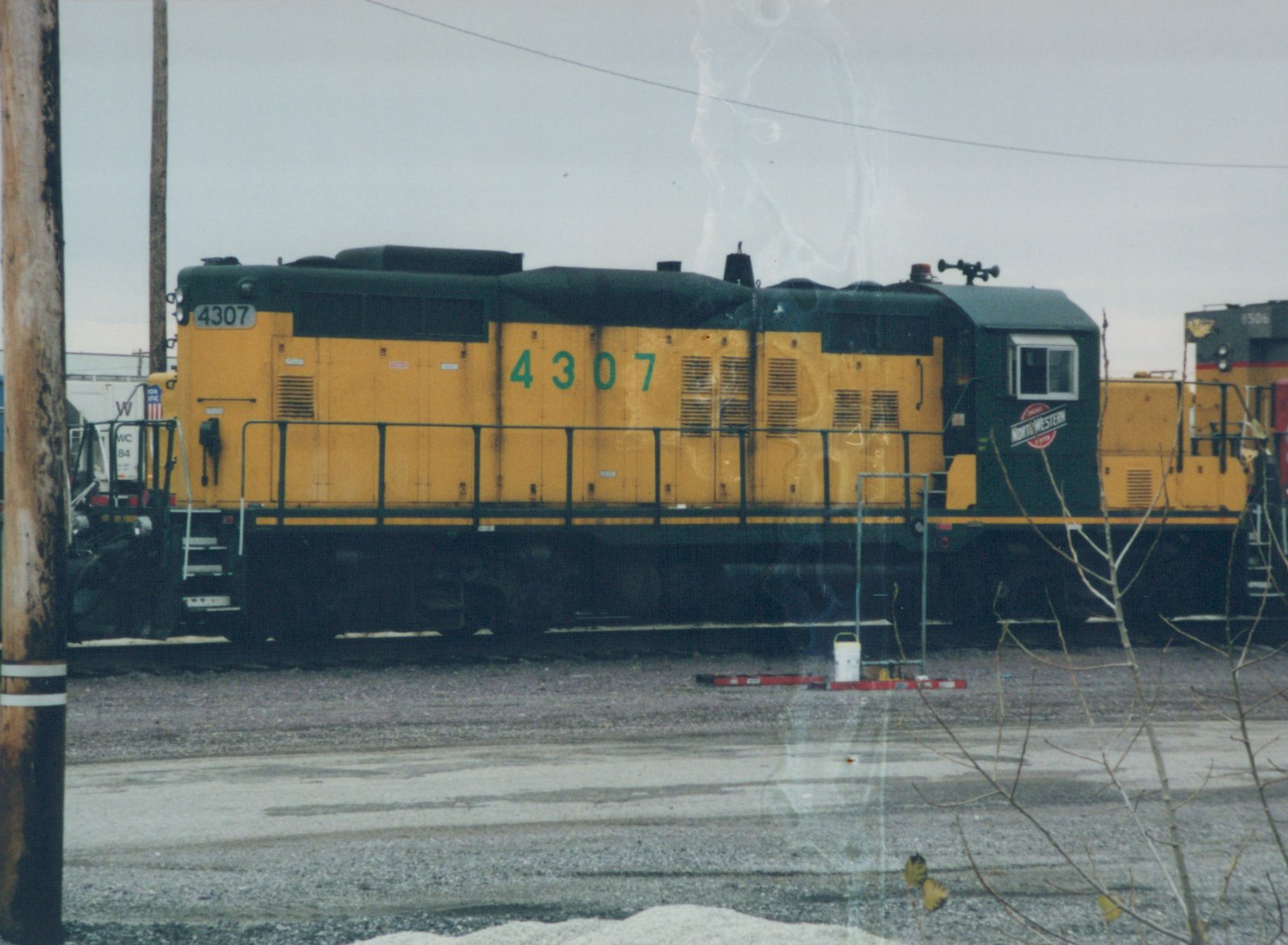 Side view of a yellow and green Chicago and North Western diesel locomotive numbered 4307, parked in a winter yard with snow on the ground.