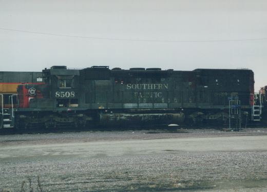 A side view of a Southern Pacific diesel locomotive, number 8508, painted black and standing in a gravel rail yard on a cloudy day.