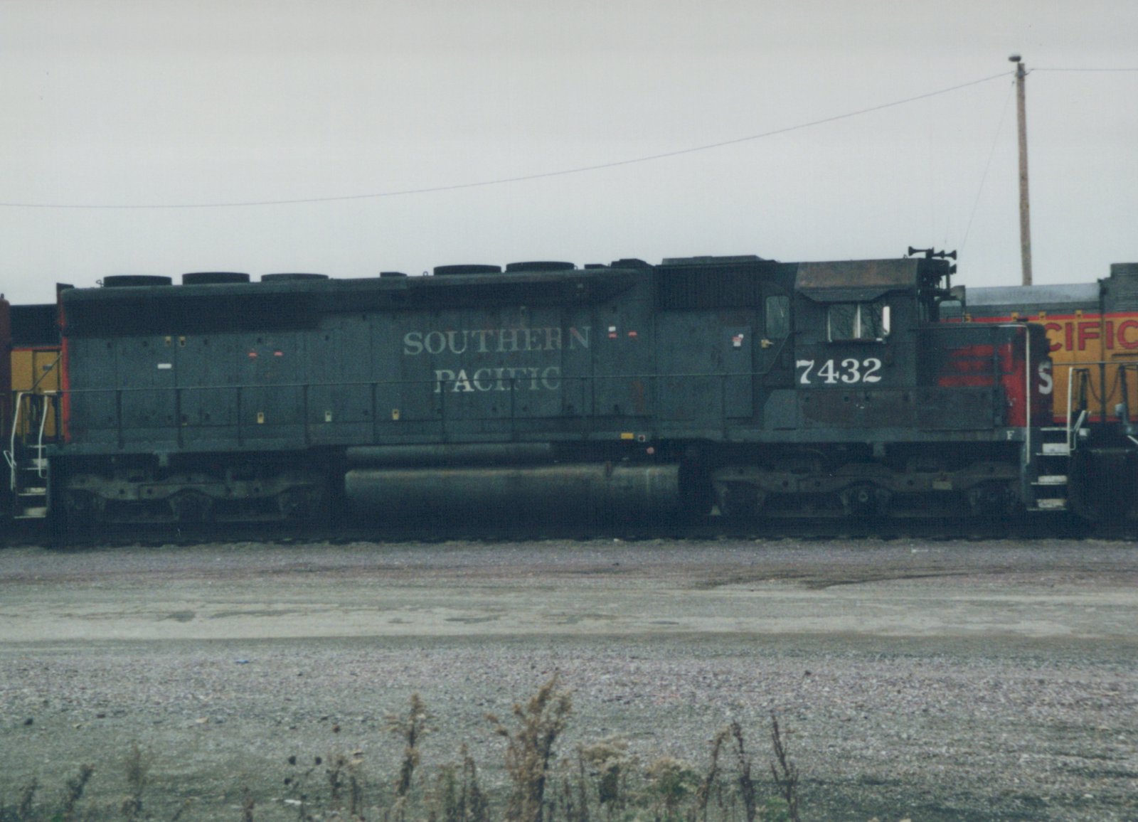 A side-view photograph of a Southern Pacific diesel locomotive, number 7432, painted in dark green with a red nose, standing in a gravel yard.