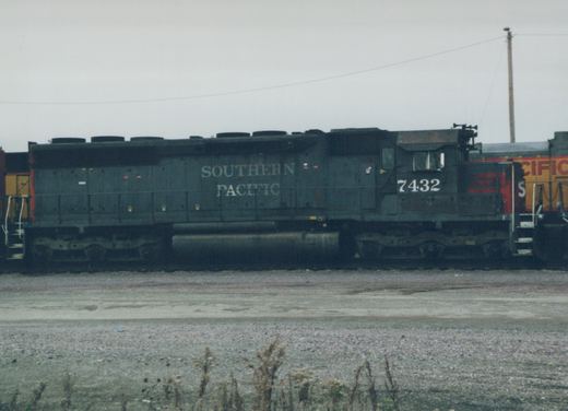 A side-view photograph of a Southern Pacific diesel locomotive, number 7432, painted in dark green with a red nose, standing in a gravel yard.