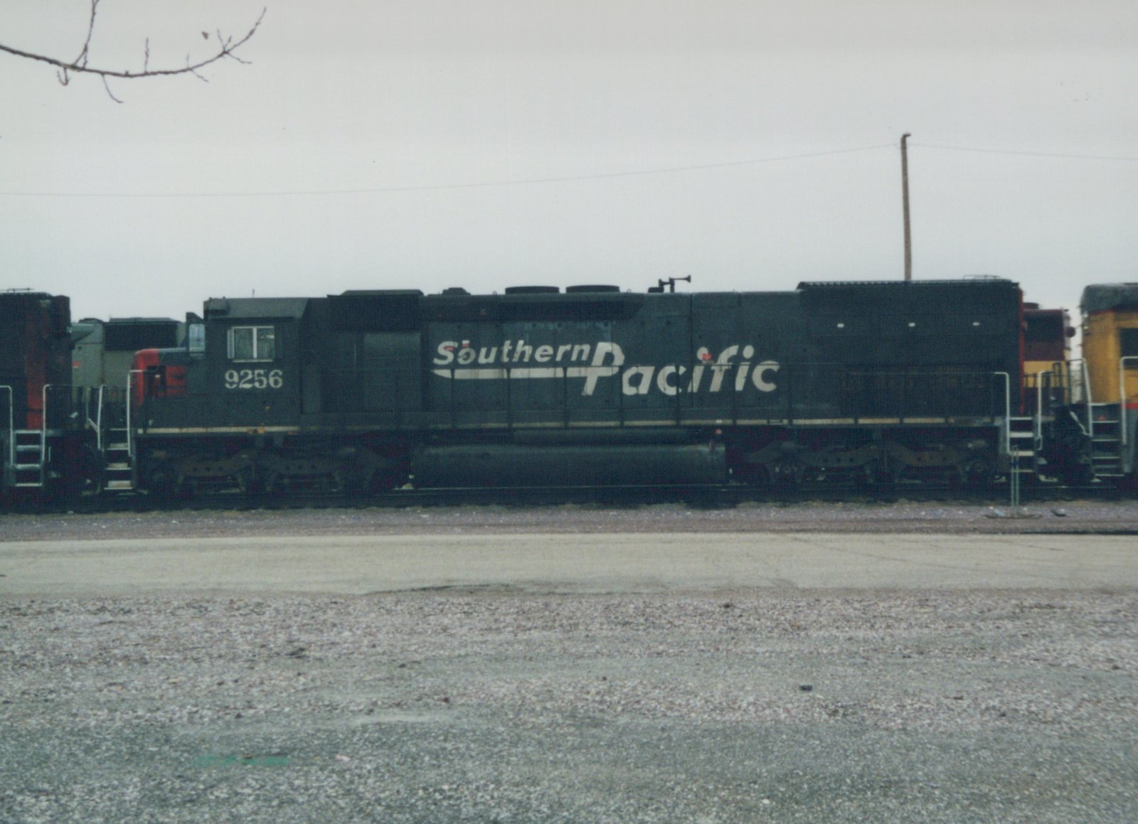 Side view of a Southern Pacific diesel locomotive, number 9256, standing on tracks in a gravel yard under a gray sky.