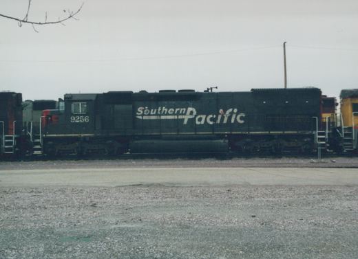 Side view of a Southern Pacific diesel locomotive, number 9256, standing on tracks in a gravel yard under a gray sky.