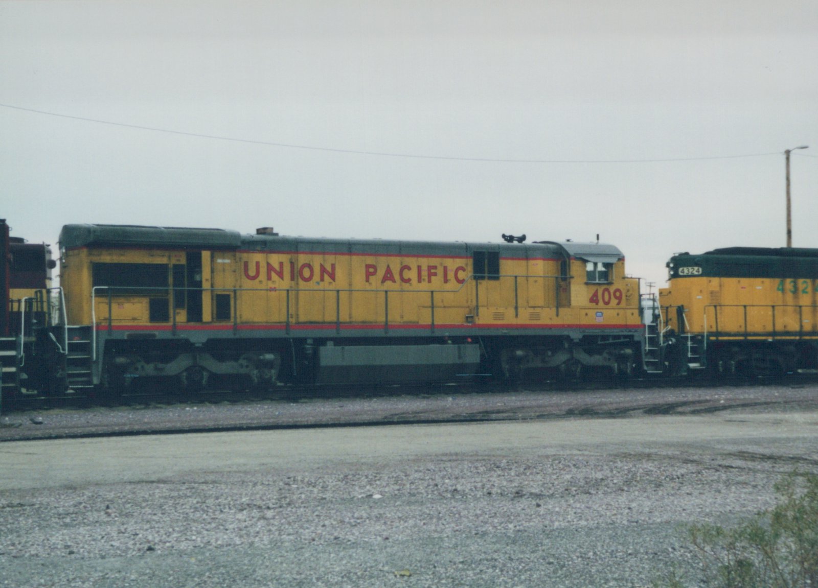 Two Union Pacific diesel locomotives, numbers 409 and 4324, are parked side by side in a gravel rail yard under an overcast sky.