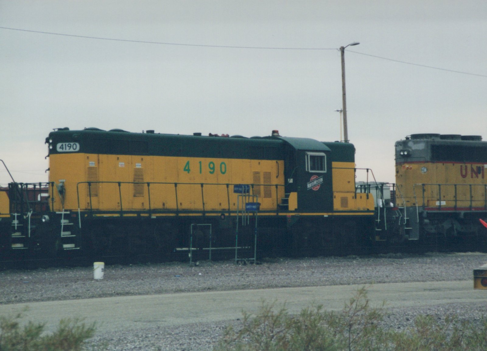 A yellow and black diesel locomotive with the number 4190 and a Northwestern herald on its cab side is parked on a gravel lot next to another locomotive.
