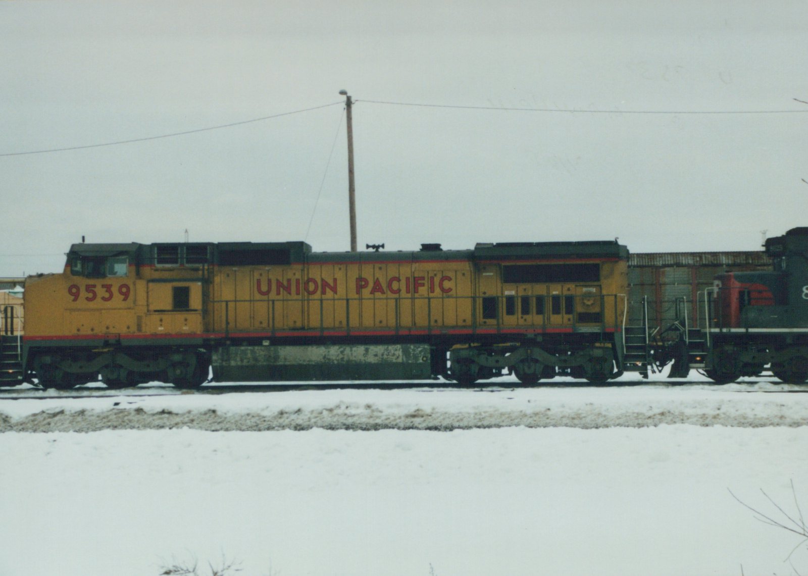 Side view of a yellow Union Pacific diesel locomotive numbered 9539 on snow-covered tracks, with another locomotive partially visible behind it.