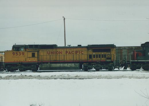 Side view of a yellow Union Pacific diesel locomotive numbered 9539 on snow-covered tracks, with another locomotive partially visible behind it.