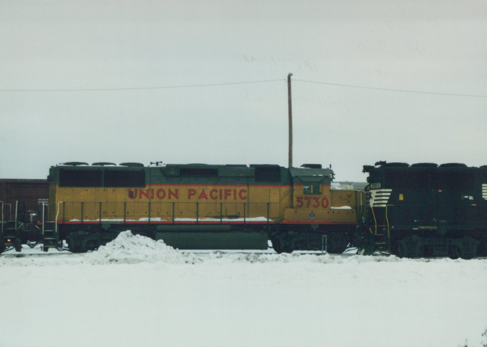 Side view of two Union Pacific diesel locomotives, 5730 and 7013, coupled on a snow-covered track under an overcast sky.