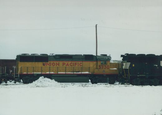 Side view of two Union Pacific diesel locomotives, 5730 and 7013, coupled on a snow-covered track under an overcast sky.