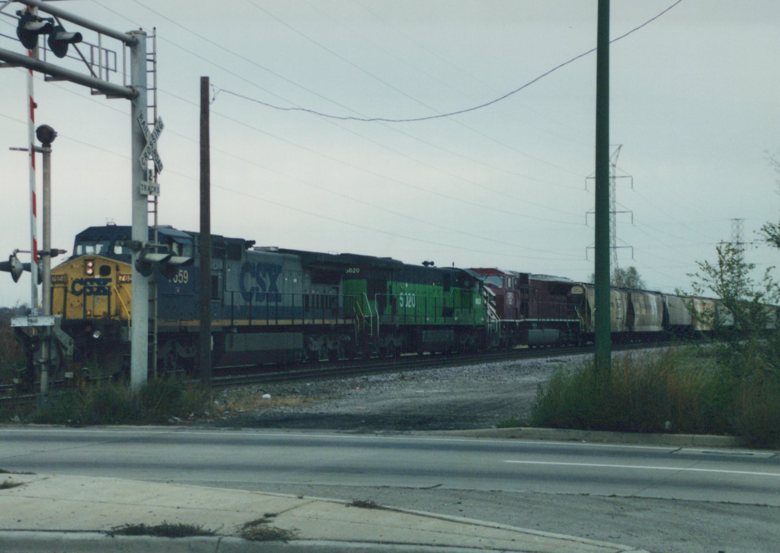 A CSX freight train with three locomotives, including number 7659 and 5020, passes a railroad crossing on an overcast autumn day.