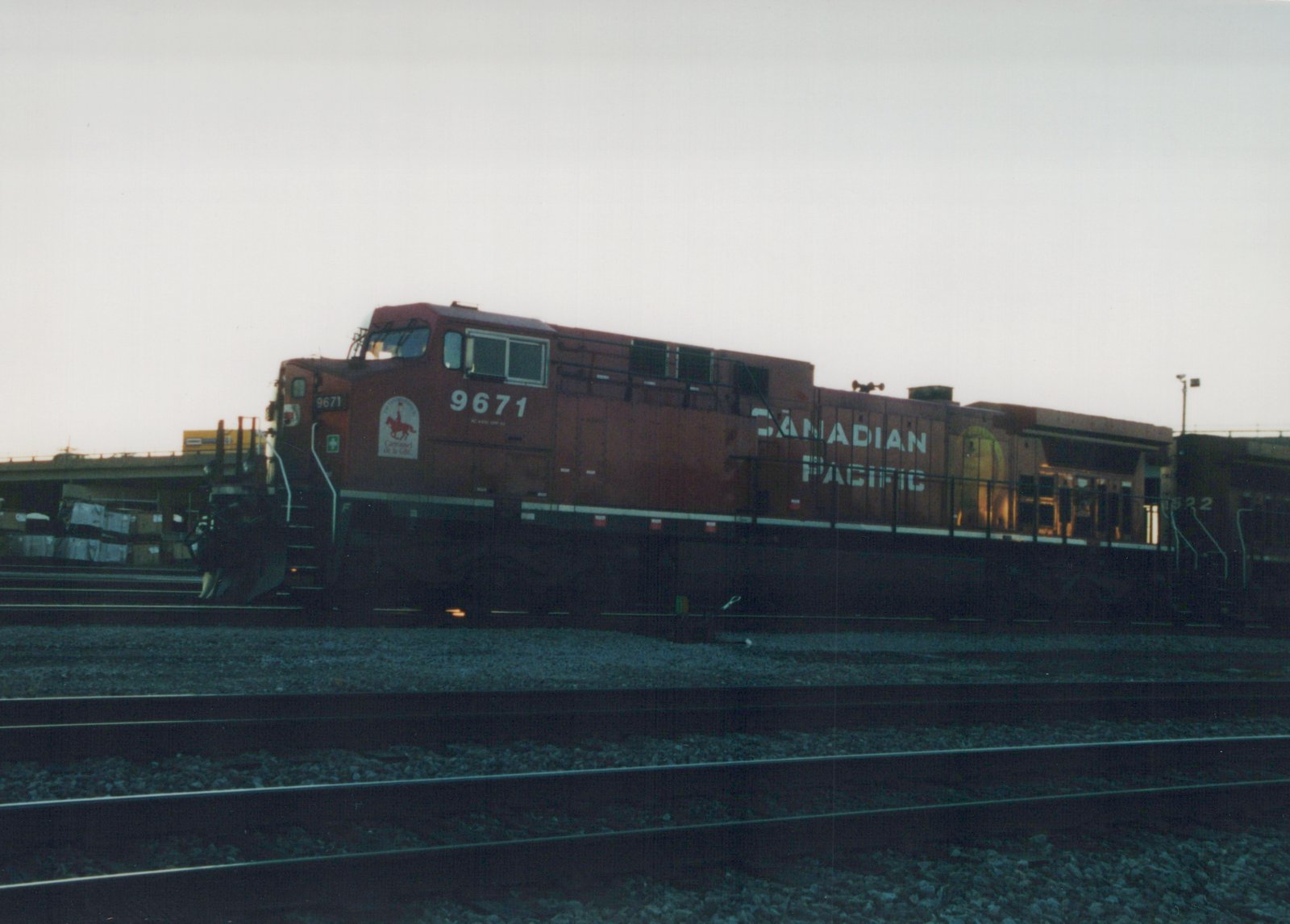 A red Canadian Pacific diesel locomotive, number 9671, sits on multiple tracks in a rail yard at dusk, with a second locomotive, number 822, visible behind it.