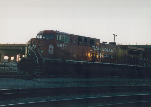A Canadian Pacific diesel locomotive, number 9671, is parked on railroad tracks at dusk, featuring a special 'Carnaval de la GRC' decal on its side, with a concrete bridge in the background.