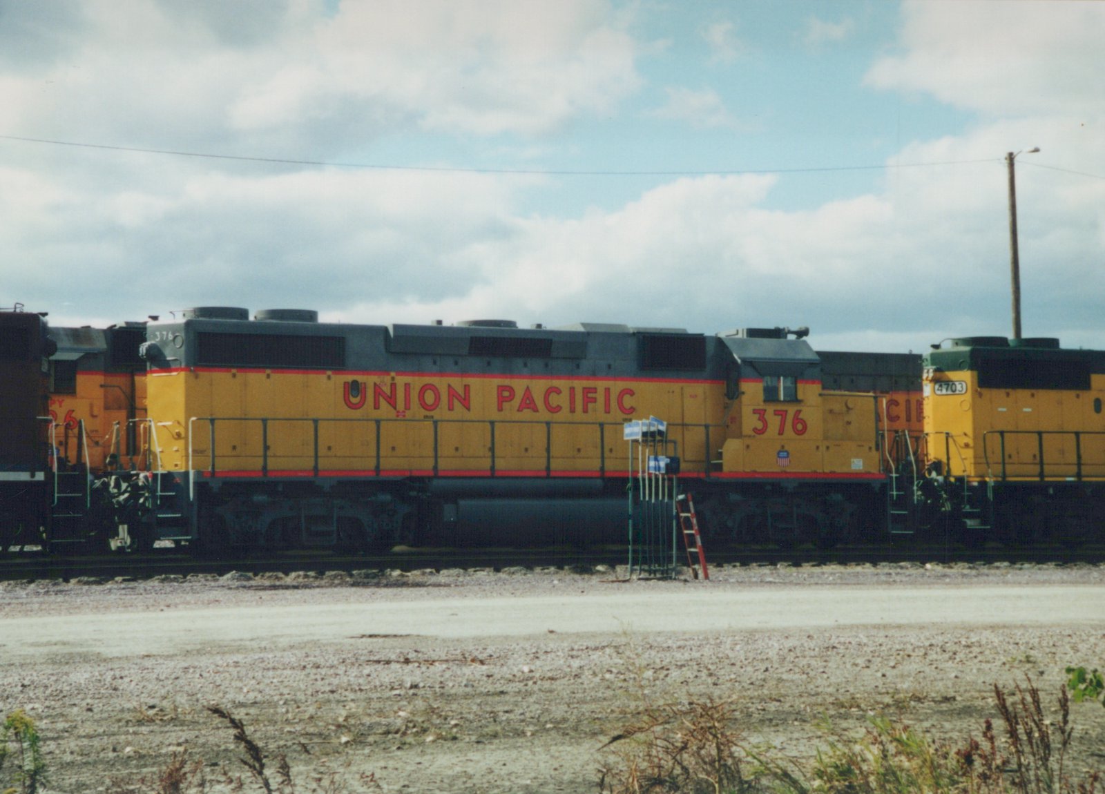 Two yellow and gray Union Pacific diesel locomotives, numbers 376 and 4703, are parked side by side on tracks in a gravel yard under a cloudy sky.