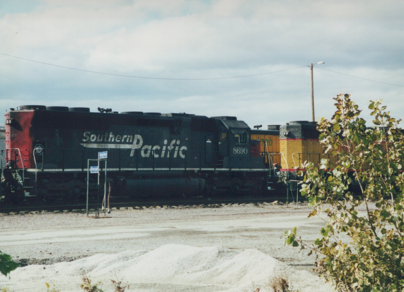 Three Southern Pacific diesel locomotives are shown side-by-side in a gravel yard under an overcast sky, with the lead unit numbered 8690.