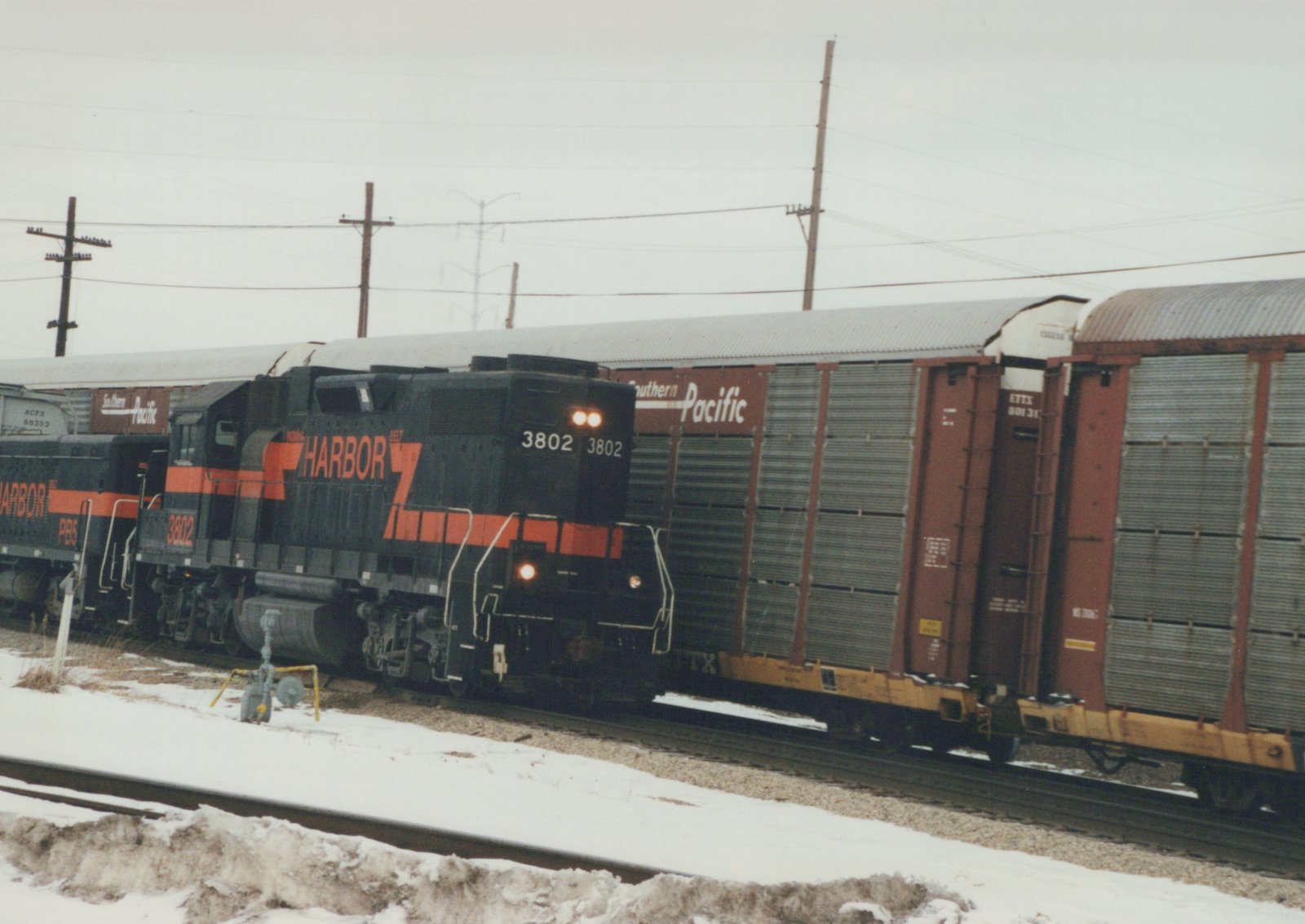 A black and orange Indiana Harbor Belt diesel locomotive, number 3802, pulls a freight train with Southern Pacific and ACF Industries cars on a snowy day.