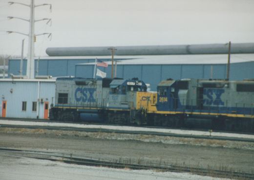 Two CSX locomotives, numbers 1517 and 2614, are parked on a track next to a blue building on an overcast winter day.