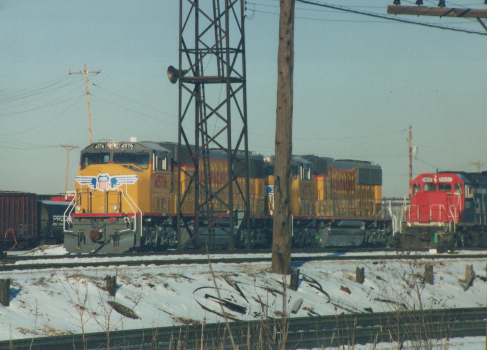 A photograph of three Union Pacific locomotives on a snowy railroad track, featuring locomotive 4576 in the lead with a yellow and gray livery, followed by locomotives 4577 and 5937.