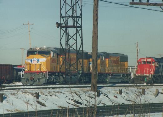 A photograph of three Union Pacific locomotives on a snowy railroad track, featuring locomotive 4576 in the lead with a yellow and gray livery, followed by locomotives 4577 and 5937.