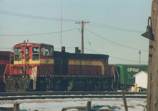 A red and yellow Canadian Pacific diesel locomotive, numbered 1436, is parked on tracks next to a green freight car in a snowy railway yard.