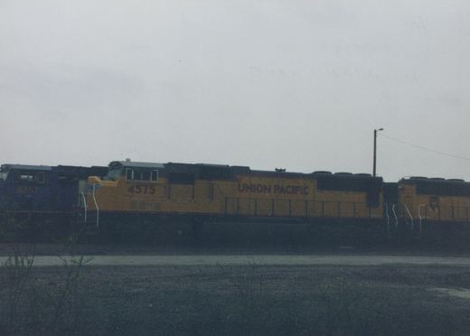 A yellow and black Union Pacific diesel locomotive, number 4575, is parked in a rail yard with another locomotive behind it under an overcast sky.