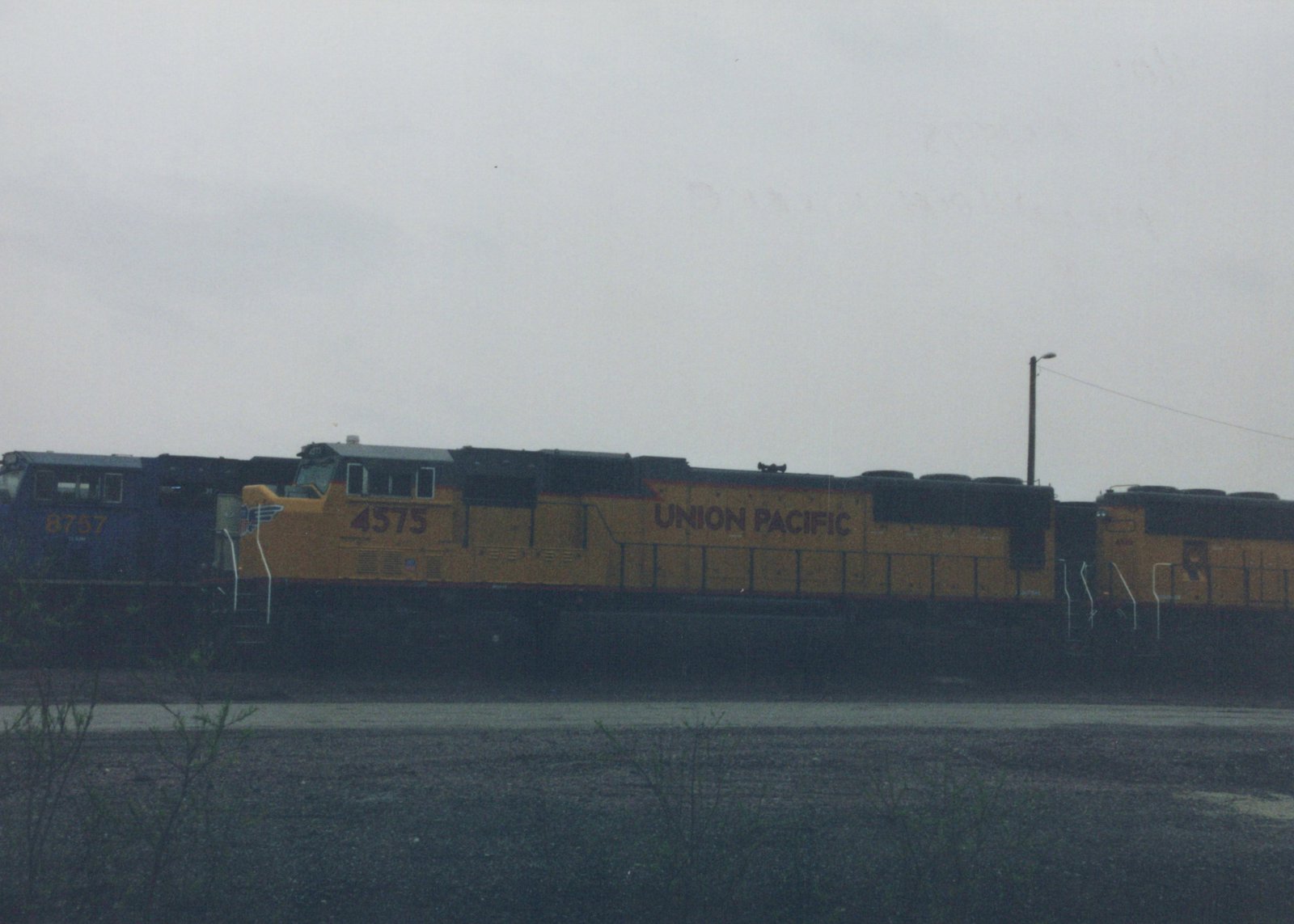 A yellow and black Union Pacific diesel locomotive, number 4575, is parked in a rail yard with another locomotive behind it under an overcast sky.