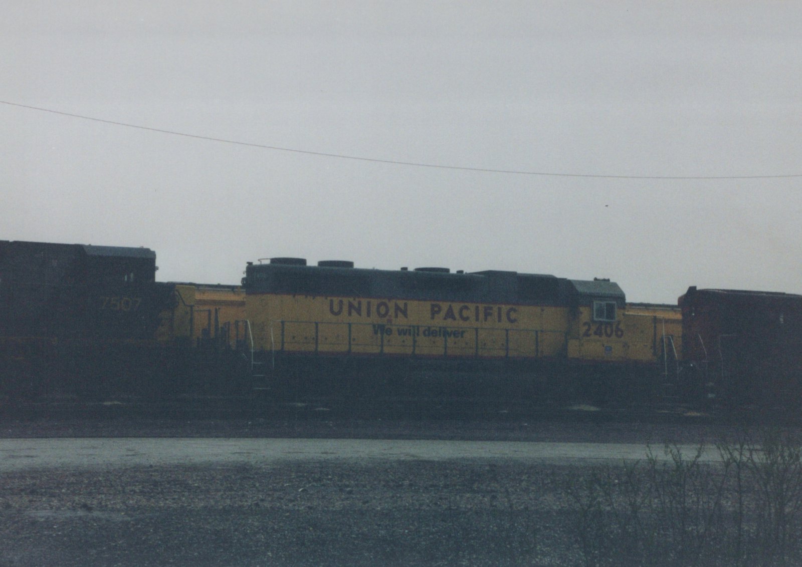 A Union Pacific diesel locomotive, number 2406, in yellow and black, sits on tracks in a rail yard under a grey sky.