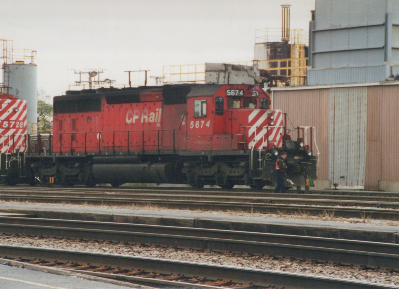 A red Canadian Pacific diesel locomotive with the number 5674 on the side is on railroad tracks with a person standing nearby.