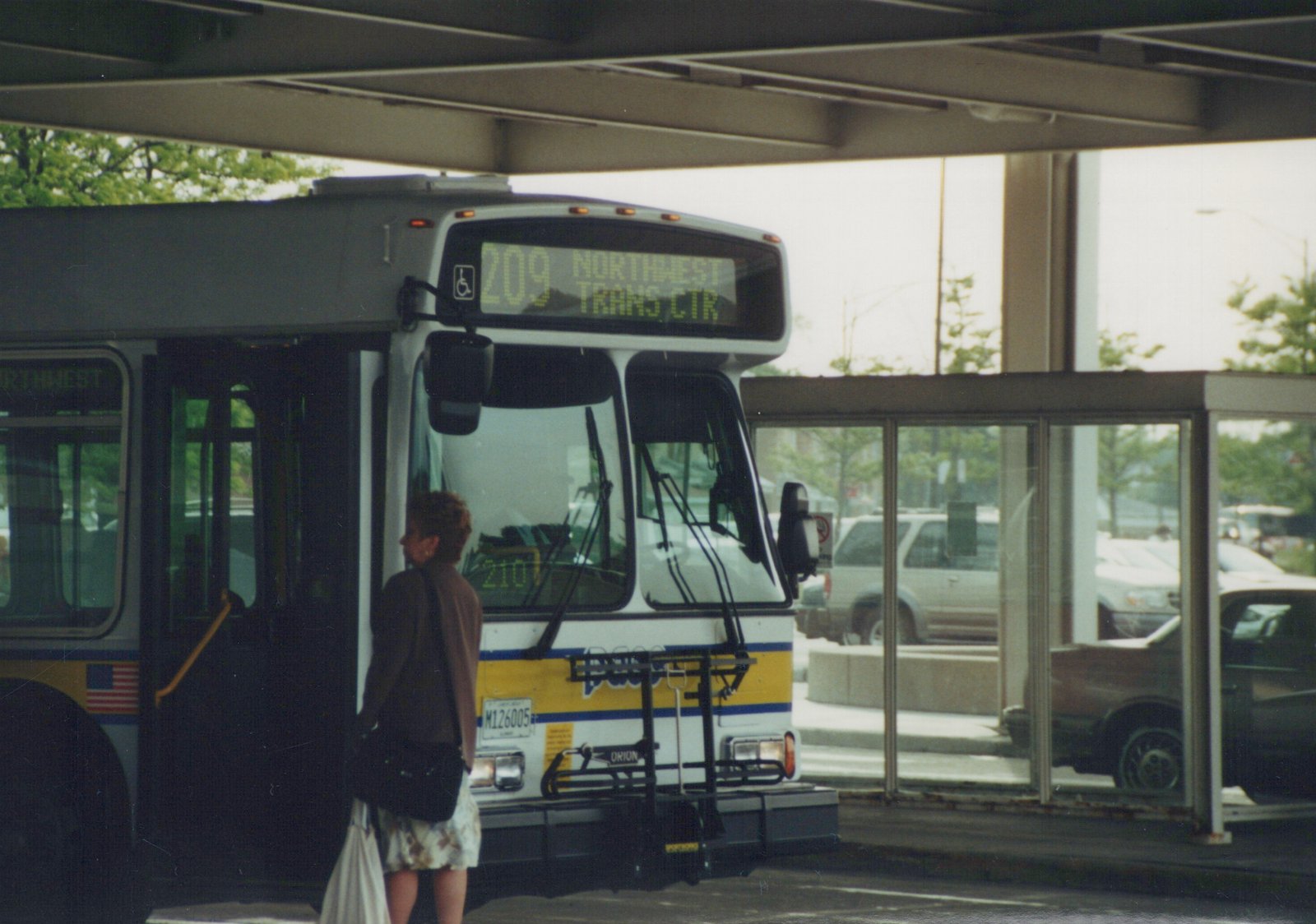 Front three-quarter view of a white and yellow Pace motor bus, number 210, stopped at a shelter with a person boarding.