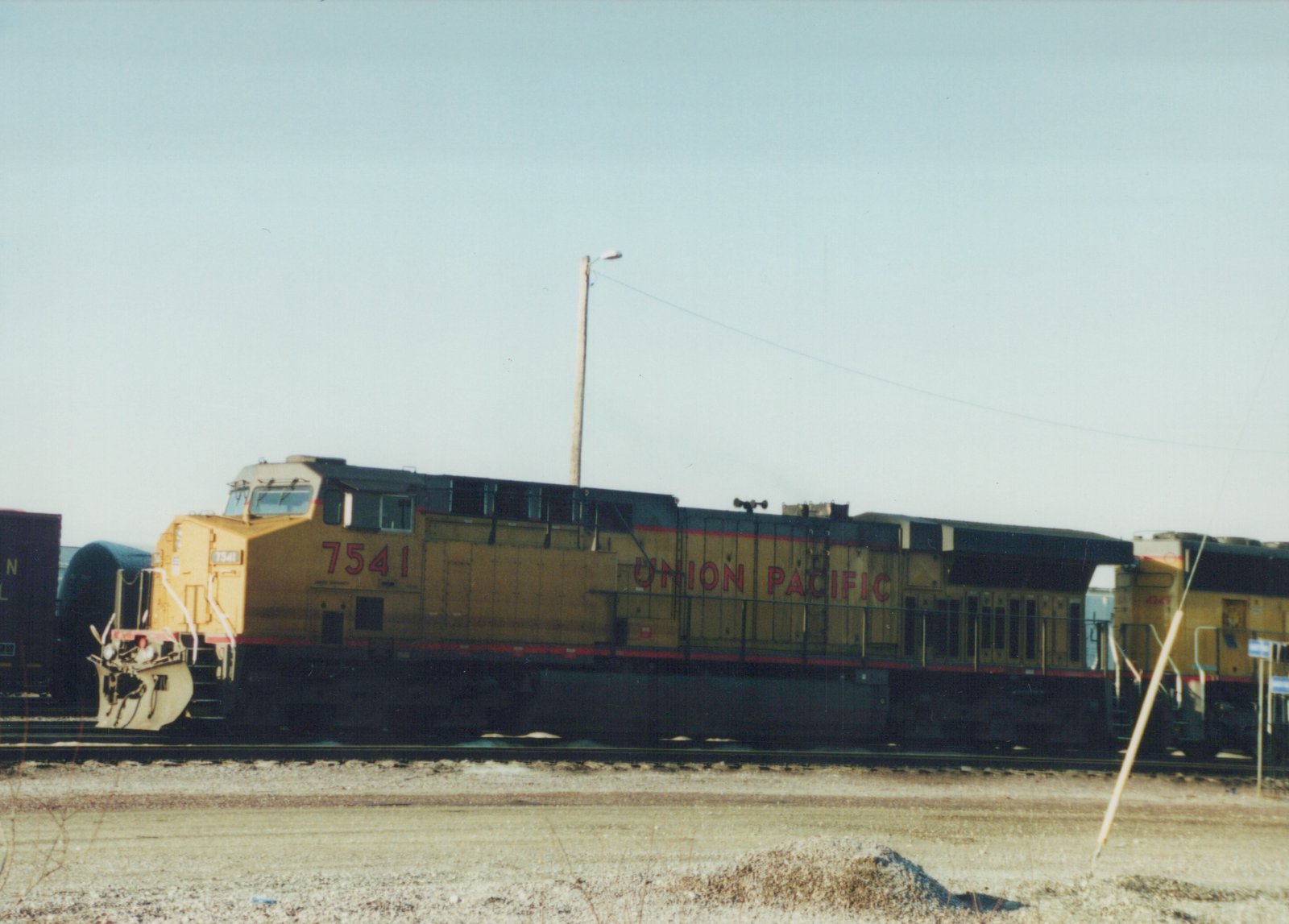 Side view of a yellow and black Union Pacific locomotive number 7541 on a set of tracks with a clear sky and a second locomotive behind it.