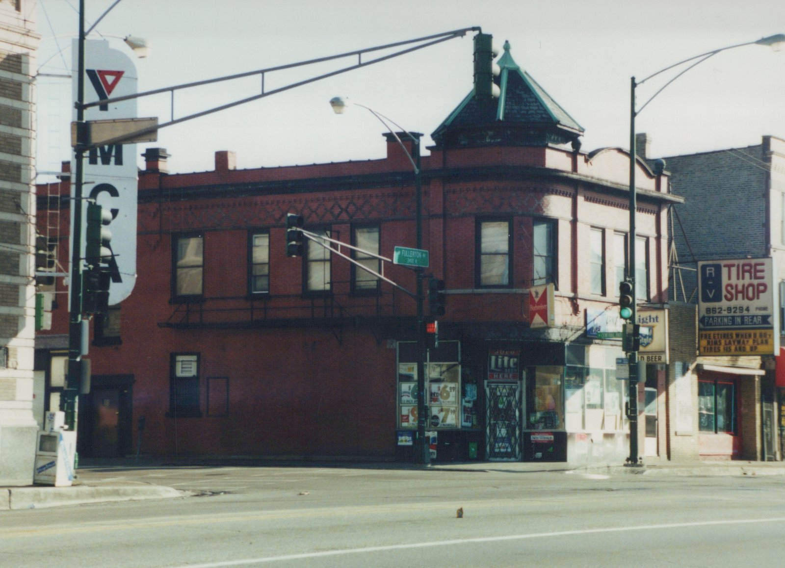 A daytime street scene at an intersection in Chicago, showing a red brick building with a tire shop and a beer store, with a street sign for Fullerton Avenue.