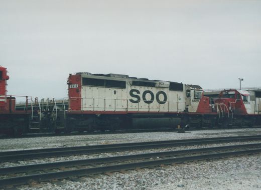 Side view of two Soo Line diesel locomotives, numbers 6610 and 6009, in white and red livery, parked on parallel tracks in a gravel yard under a grey sky.