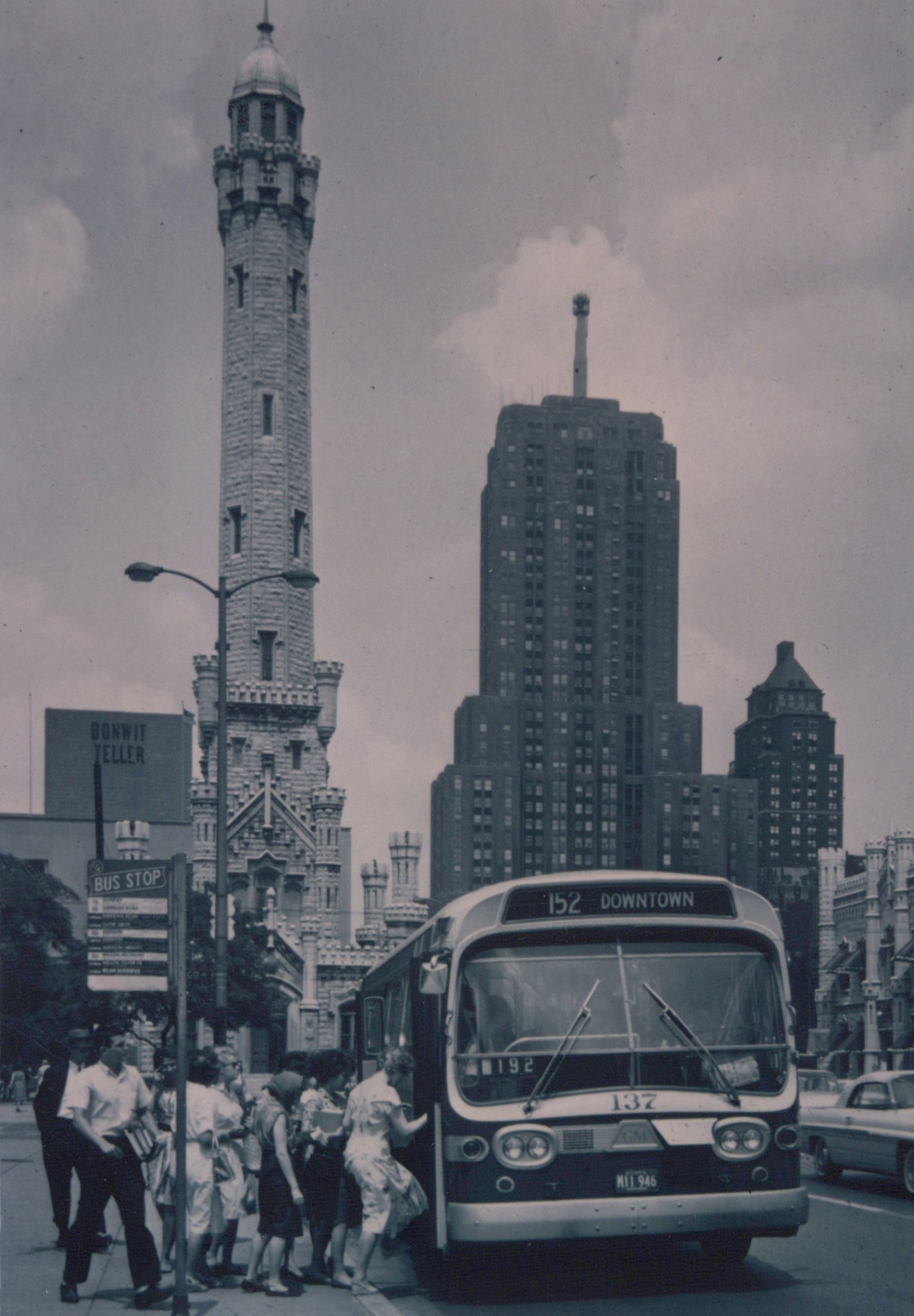 A front view of a Chicago Transit Authority bus numbered 137, parked at a curb with passengers boarding, with the Chicago Water Tower and city skyline behind it.