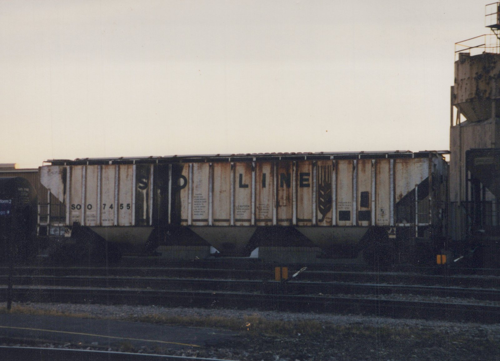 A side view of a Soo Line freight car, number 7455, parked on tracks in a rail yard during dusk.