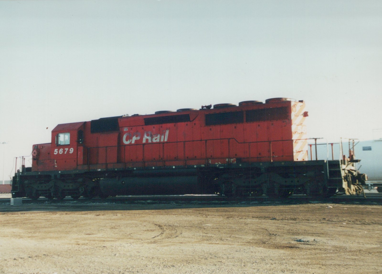 Side view of a red Canadian Pacific locomotive numbered 5679, standing on tracks in a dirt yard under an overcast sky.