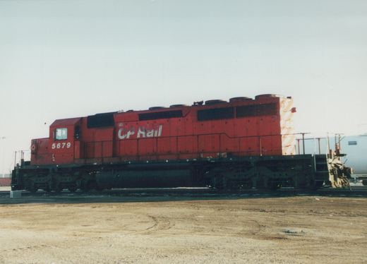 Side view of a red Canadian Pacific locomotive numbered 5679, standing on tracks in a dirt yard under an overcast sky.