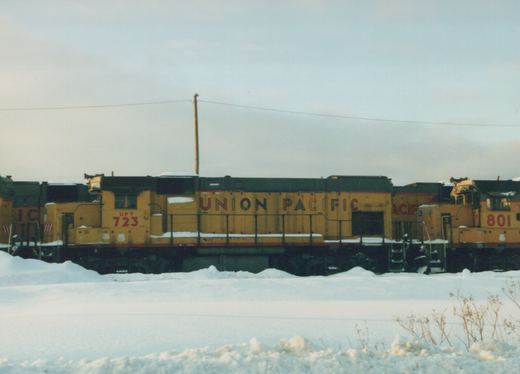 Two yellow Union Pacific diesel locomotives, numbered 723 and 801, standing side by side on a snow-covered railroad track under an overcast sky.