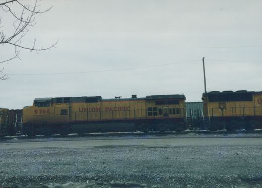 Side view of a yellow Union Pacific diesel locomotive no. 9768 with 'UNION PACIFIC' lettering on its side, positioned on a track in a gravel yard under an overcast sky.