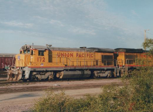 Side view of two Union Pacific GP9 diesel locomotives, numbers 172 and 517, in yellow and red livery, standing on tracks in a yard with a boxcar in the background.
