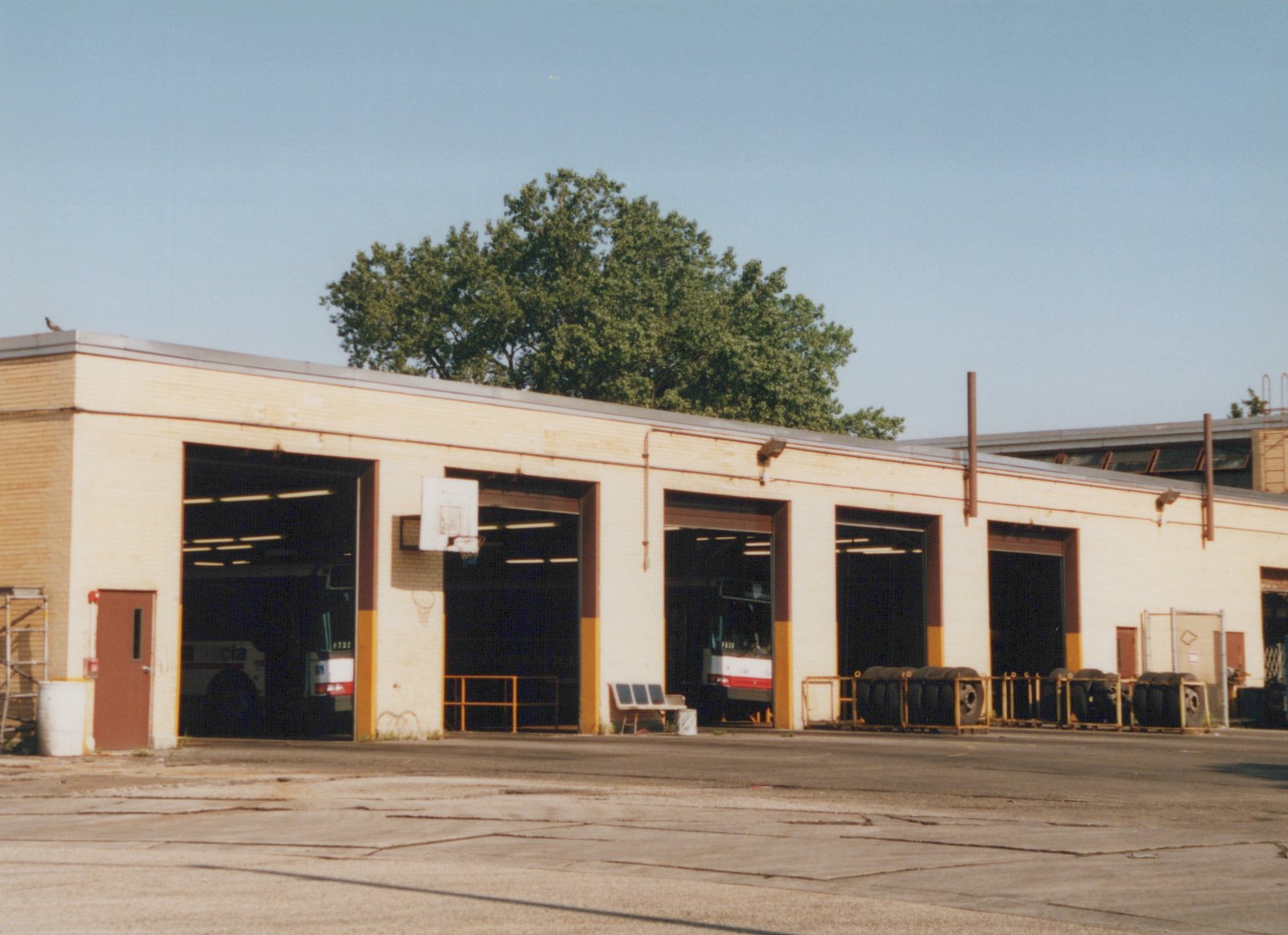 A long, light-colored brick building with several large garage doors, each revealing a CTA bus inside; a basketball hoop is mounted on the exterior wall, and large tires are stacked outside.