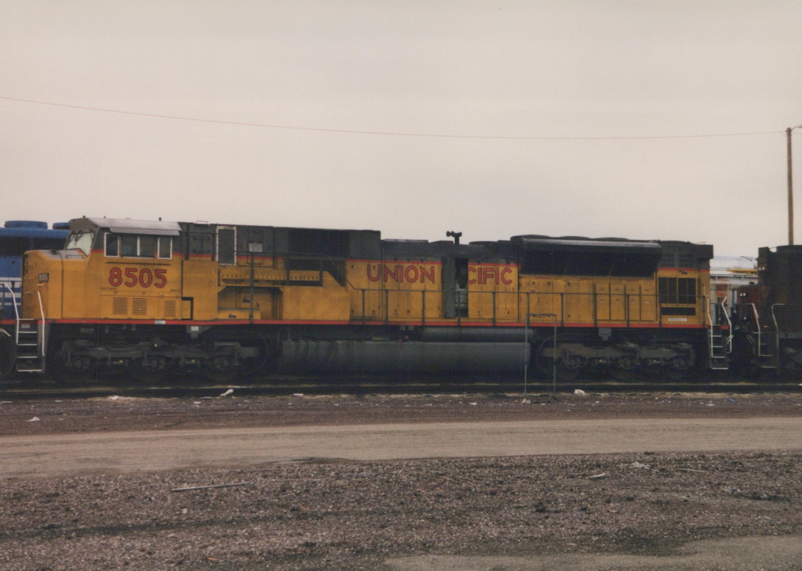 Side view of a yellow Union Pacific locomotive numbered 8505, parked on tracks in a gravel yard with overcast skies.