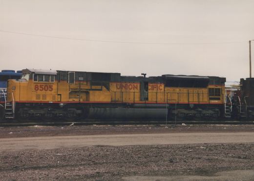 Side view of a yellow Union Pacific locomotive numbered 8505, parked on tracks in a gravel yard with overcast skies.