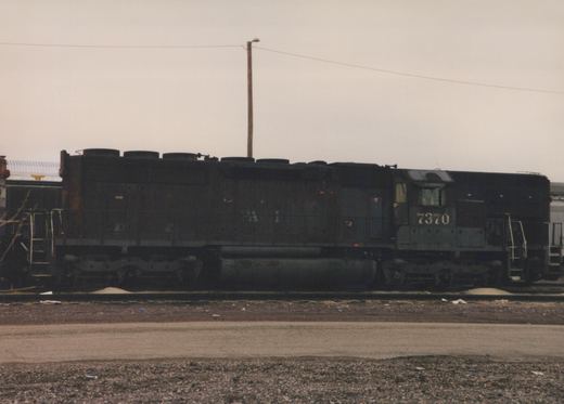 A black Southern Pacific diesel locomotive, number 7370, sits on tracks in a gravel yard on a cloudy day.