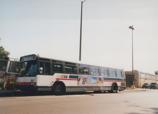 Side view of a white Chicago Transit Authority bus with red and blue stripes, number 5574, parked in a lot with another bus and trucks nearby.