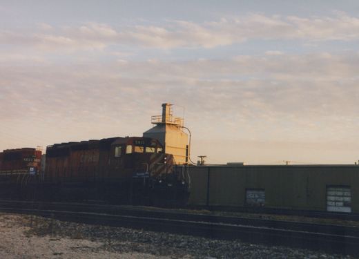 A Canadian Pacific diesel locomotive, number 5913, is parked on railroad tracks next to a warehouse as the sun sets.
