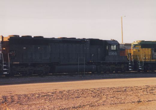 A side view of a black Southern Pacific locomotive, number 7504, in a rail yard, with a yellow and green SP locomotive, number 5535, partially visible beside it.