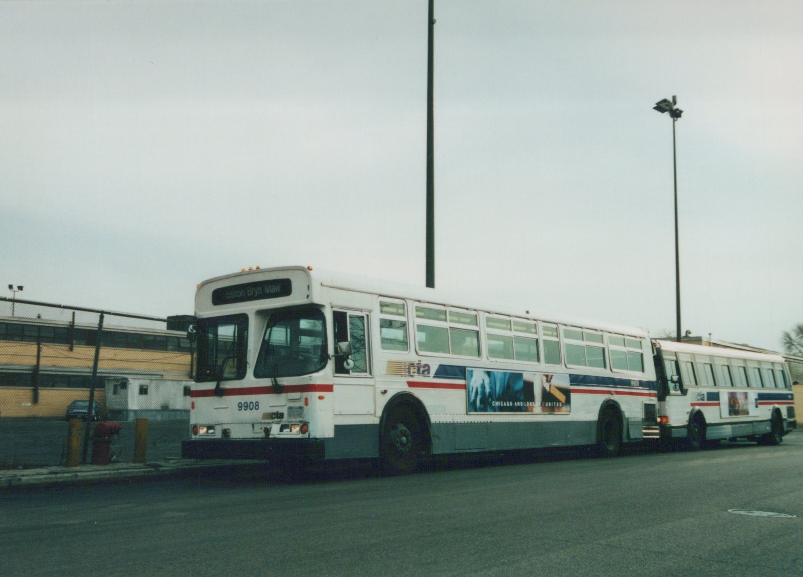 Two white Chicago Transit Authority buses with red and blue stripes are parked side by side on a street, with one displaying the destination 'Elston Bryn Maw' and the number 9908 on its front.