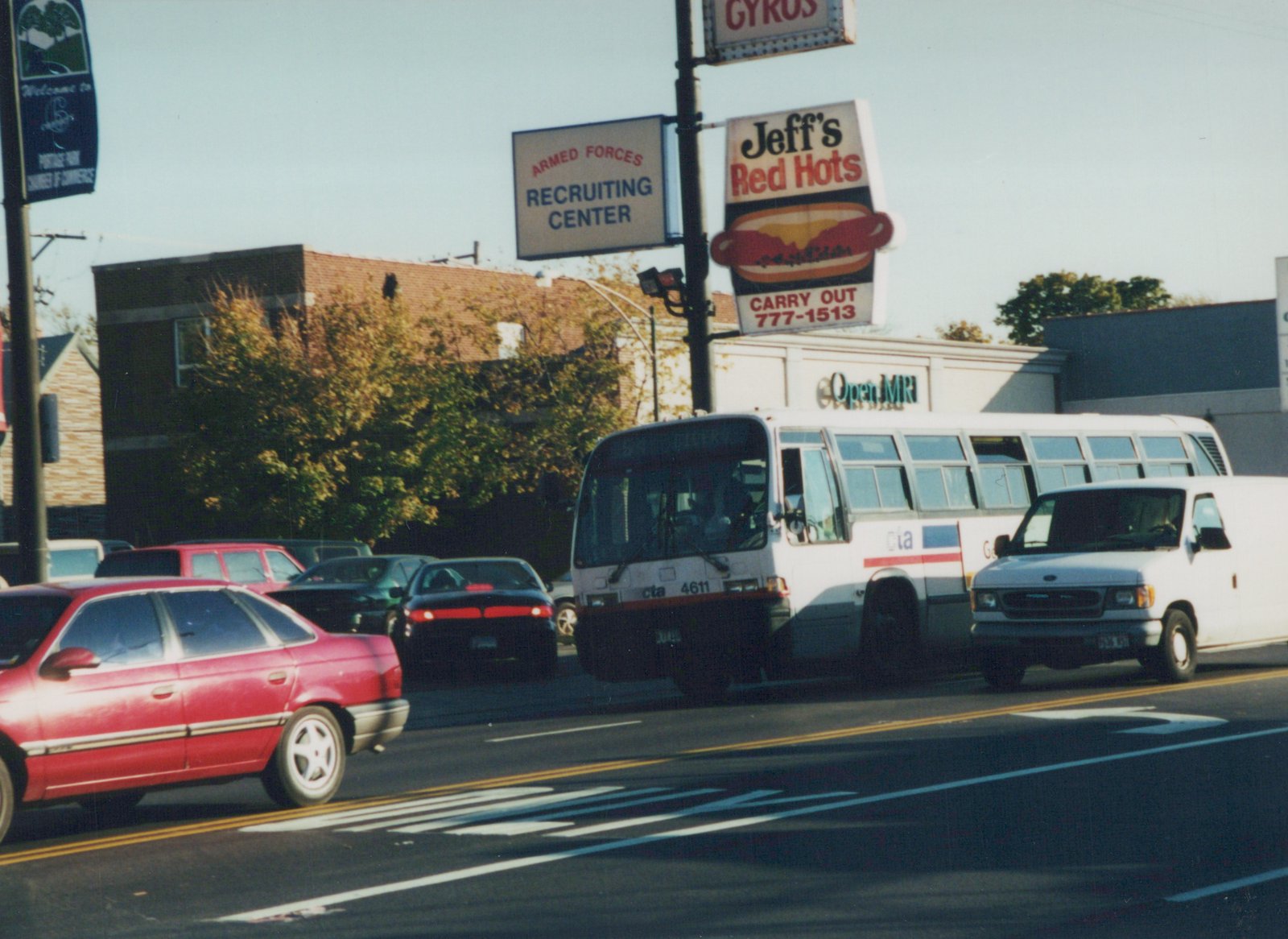A white CTA bus with red and blue stripes, numbered 4611, drives on a busy street with other cars, with signs for 'Jeff's Red Hots' and an 'Armed Forces Recruiting Center' visible in the background.