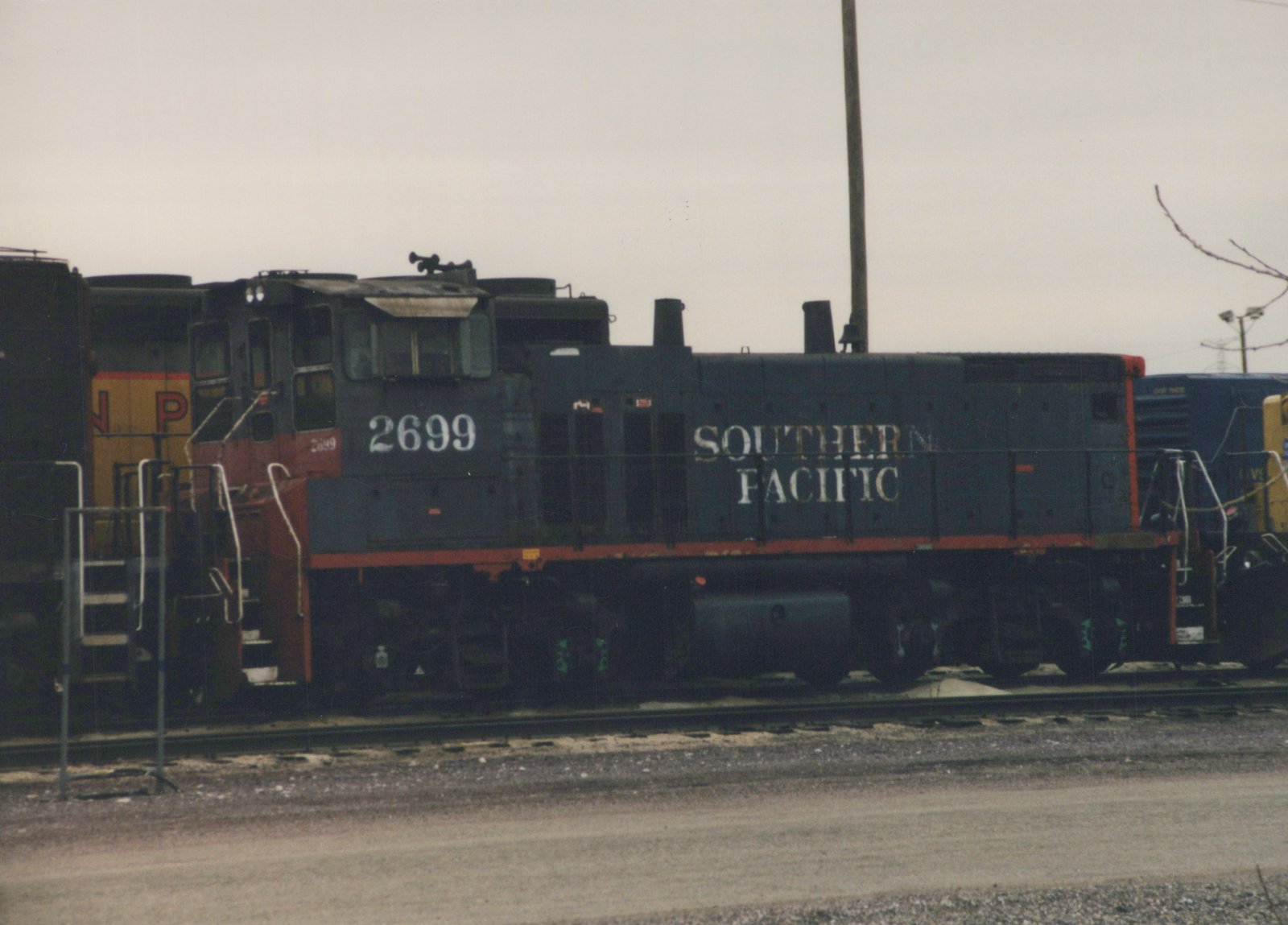 A side view of a dark gray Southern Pacific locomotive, number 2699, sitting on tracks in a yard with other locomotives partially visible behind it.