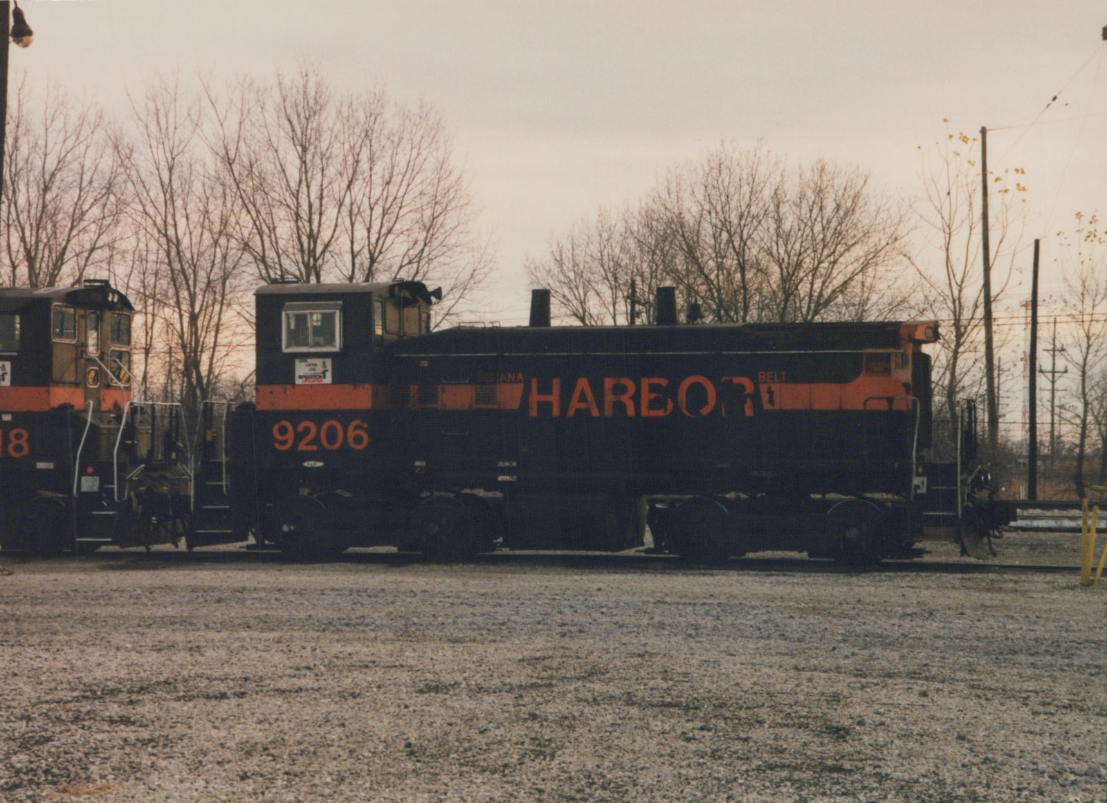Side view of a black and orange Indiana Harbor Belt diesel locomotive numbered 9206, parked on tracks in a gravel yard with bare trees in the background.
