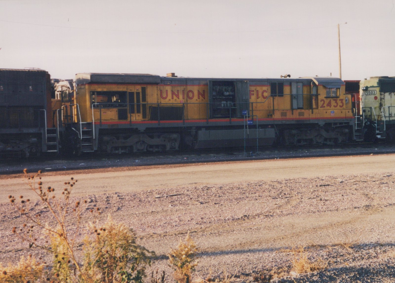 A yellow and gray Union Pacific diesel locomotive with the number 2433, parked on tracks in a rail yard with another locomotive visible behind it.