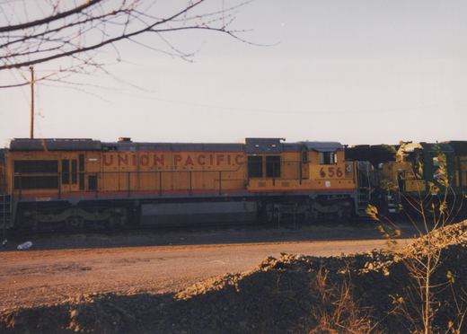 A yellow and grey Union Pacific locomotive numbered 656 is parked on railroad tracks in a yard with bare trees in the background during winter dusk.